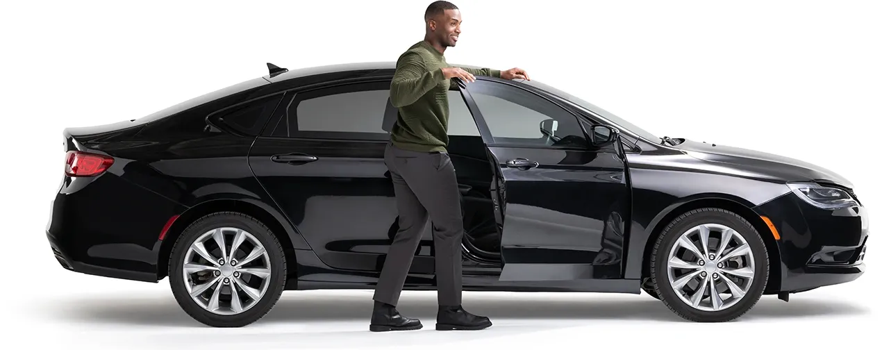 A young man stands by the open door of his midnight black car.